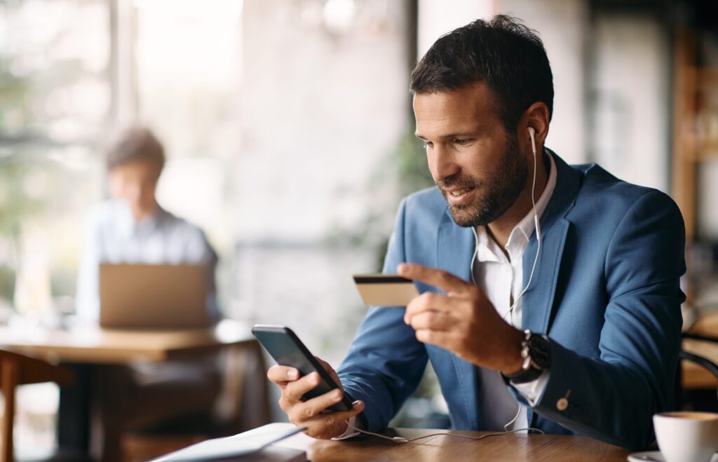 Un trabajador procede a realizar un pago online mientras toma café en una cafetería.