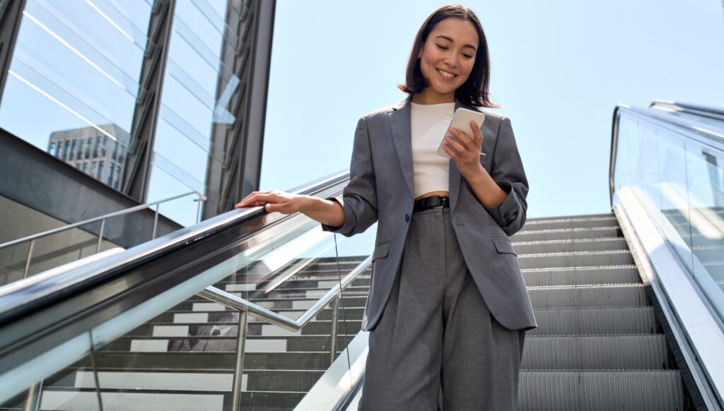 Ejecutiva consulta su móvil mientras sube a unas escaleras mecánicas en la calle.