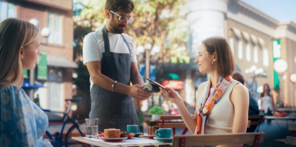 Dos mujeres pagan usando contactless al camarero del bar.