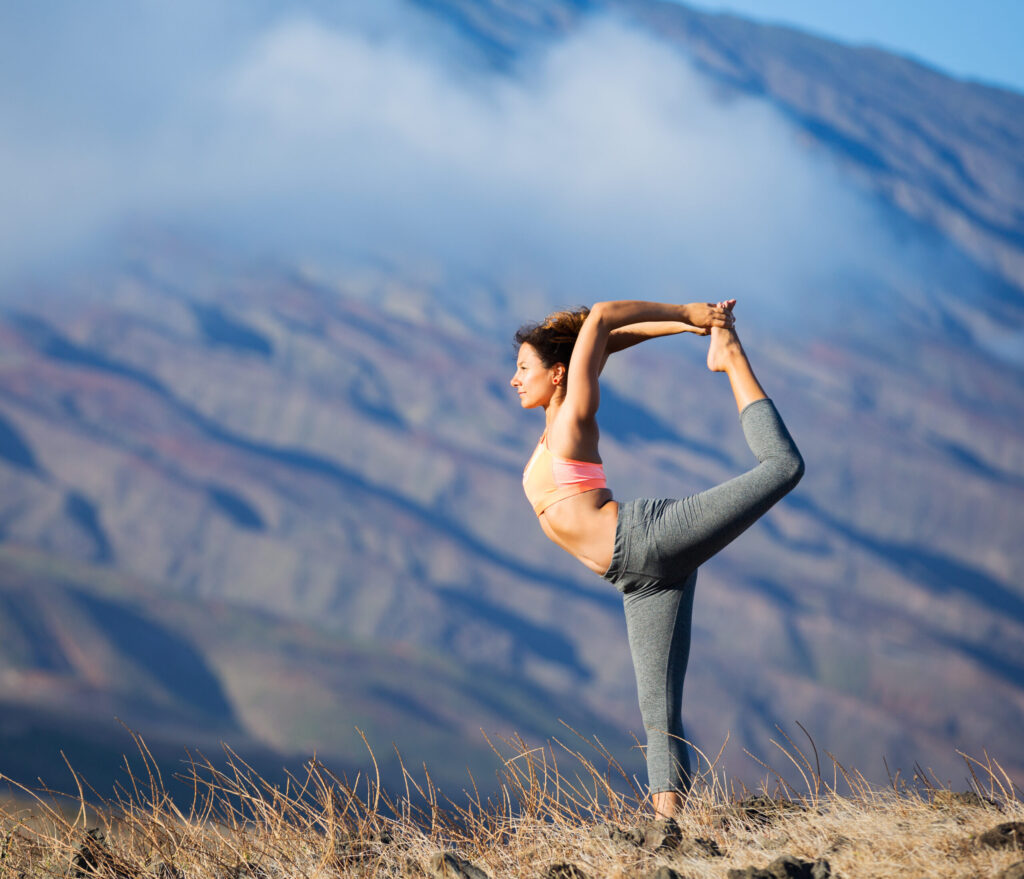 Mujer practicando yoga al aire libre con una montaña de fondo.